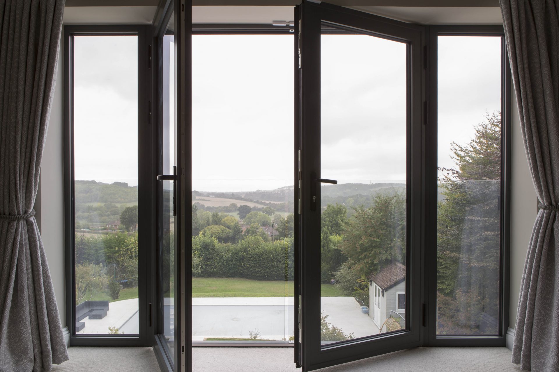 modern glass bifold door partially open, leading to a scenic countryside view. The dark-framed doors have large glass panels, allowing natural light to enter the room